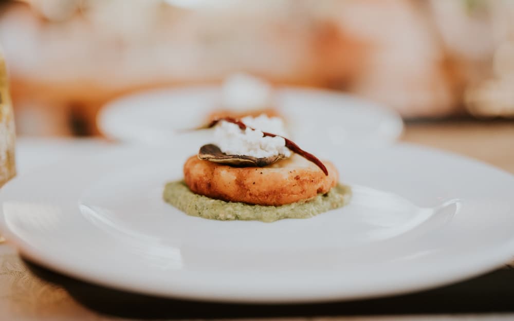 Antipasto gourmet: tortino dorato su crema verde, con ricotta e una chip croccante, su piatto bianco