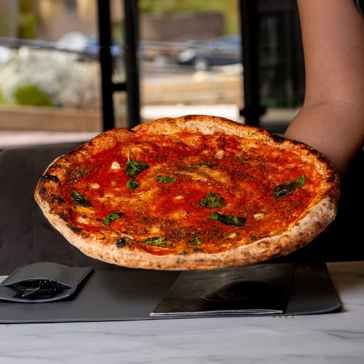 Pizza rossa con pomodoro ed erbe fresche, servita a mano sopra il tavolo