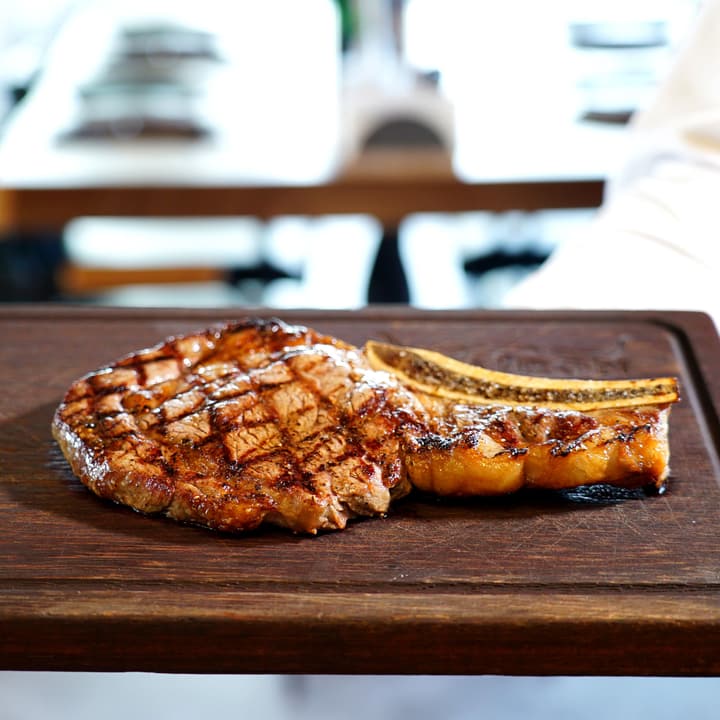 Bistecca con l’osso segnata dalla griglia, servita su un tagliere di legno scuro