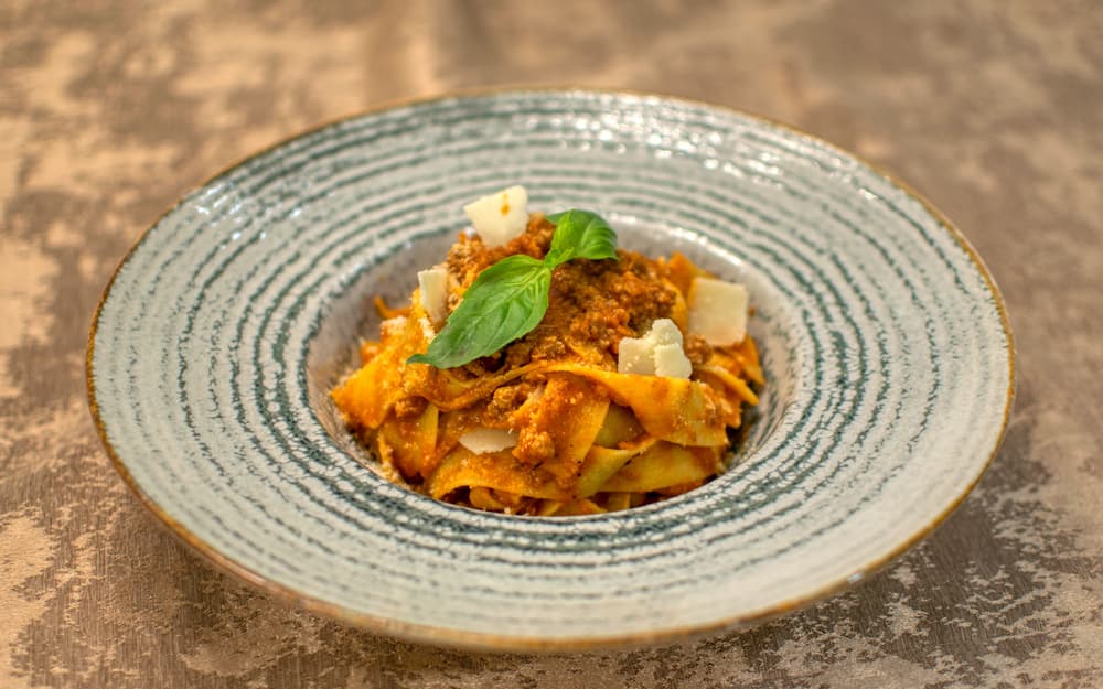 Pappardelle al ragù con basilico e scaglie di formaggio, in una fondina di ceramica rigata
