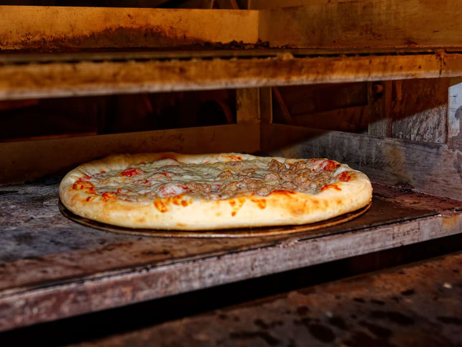 Una pizza in cottura nel forno, appoggiata sul piano di acciaio