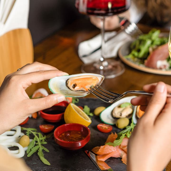 Antipasto di mare condiviso: cozze, calamari, salmone e olive su un tagliere di ardesia