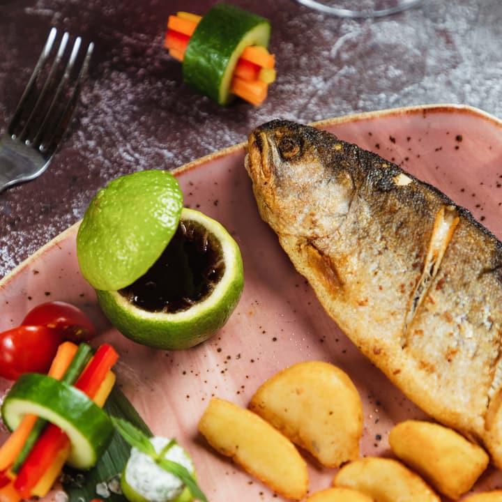 Pesce intero al forno con patate, verdure e lime, servito su un piatto rosa