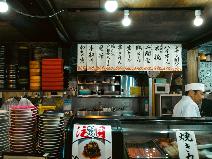 Il bancone di un locale giapponese con i menu appesi, le pile di piatti e il personale al lavoro