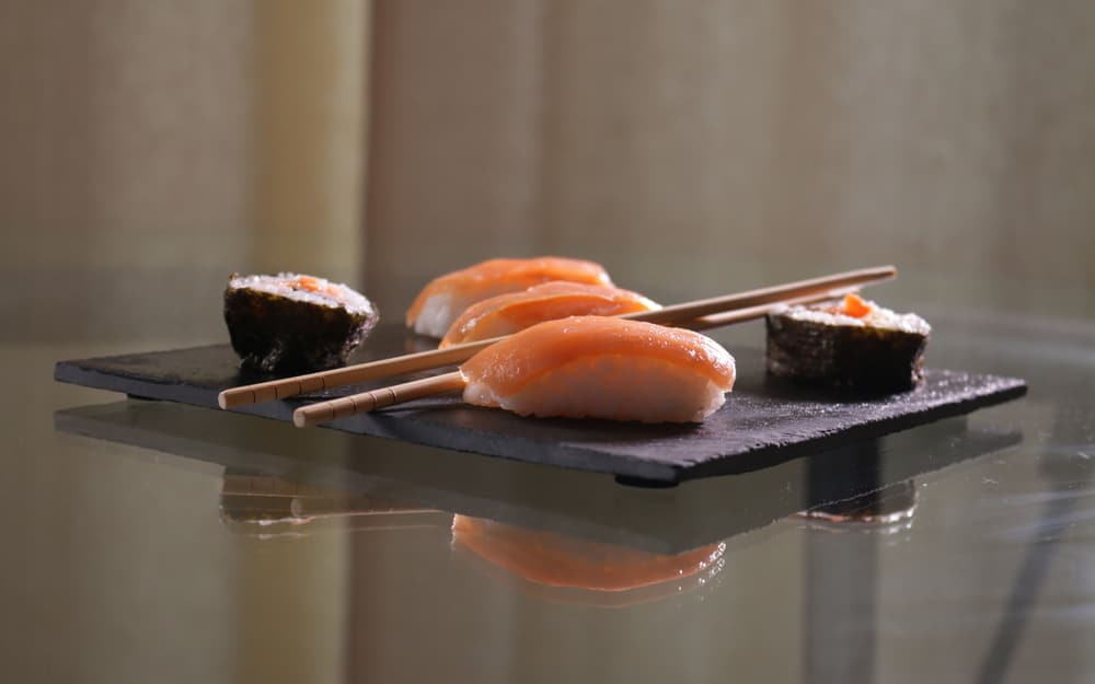 Nigiri di salmone e due maki su una lastra di ardesia, con le bacchette appoggiate di lato