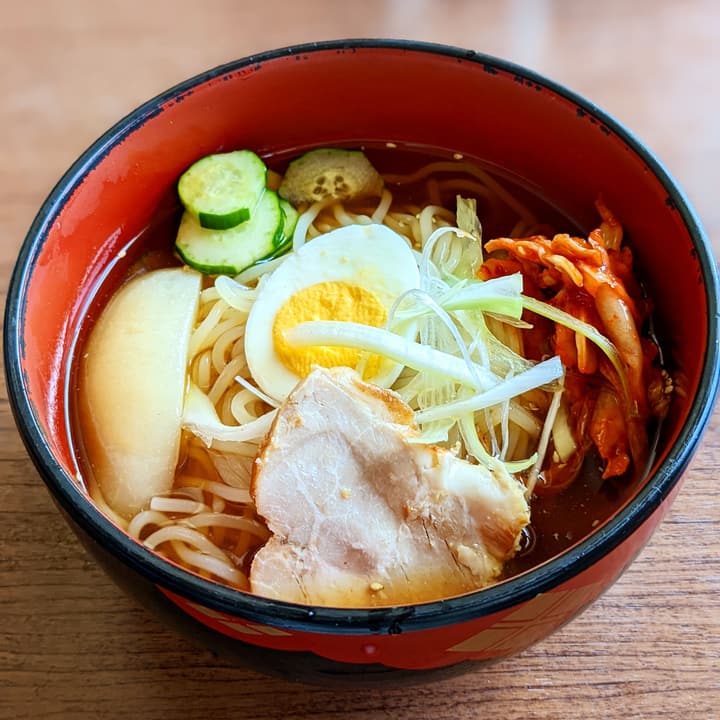 Ciotola laccata di ramen con uovo sodo, fetta di maiale, kimchi e cetriolo
