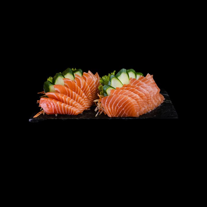 Fette di sashimi di salmone disposte a ventaglio su ardesia, con cetriolo e insalata